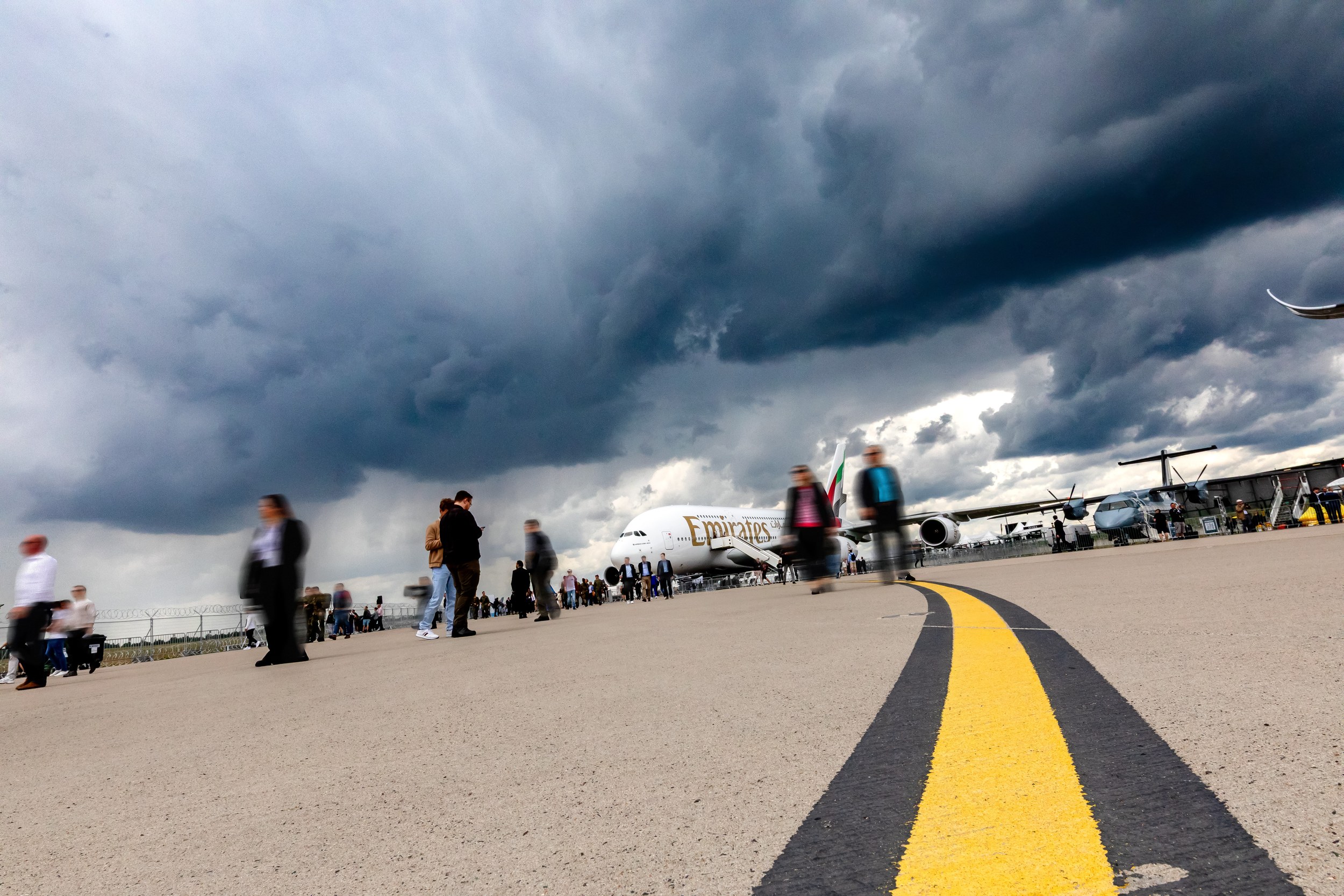 An Emirates Airbus A380-800 stands in the static display behind a line of visitors on the apron.