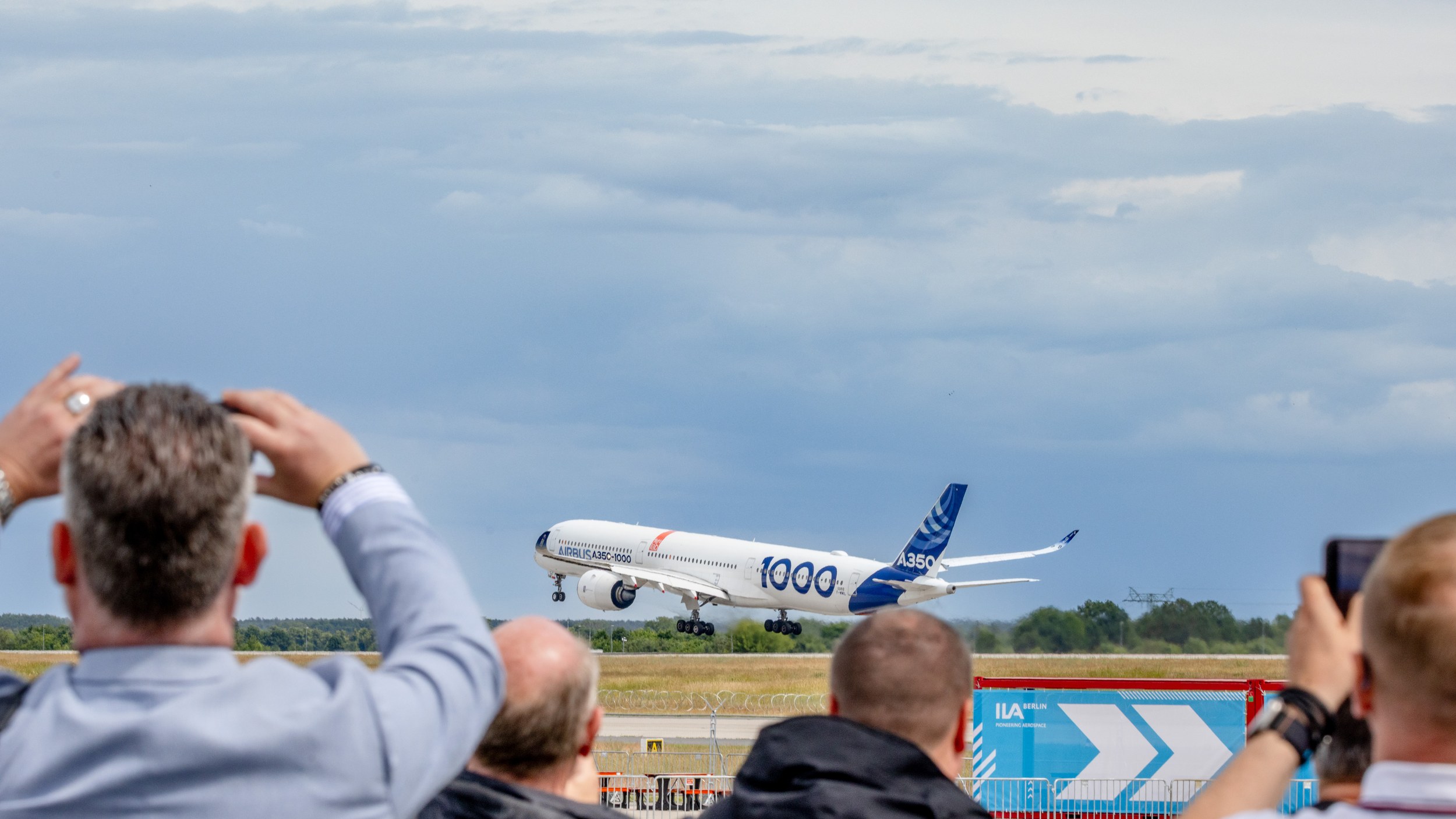 An Airbus A350-1000 lifts off from the runway with its landing gear extended in front of a row of spectators taking …
