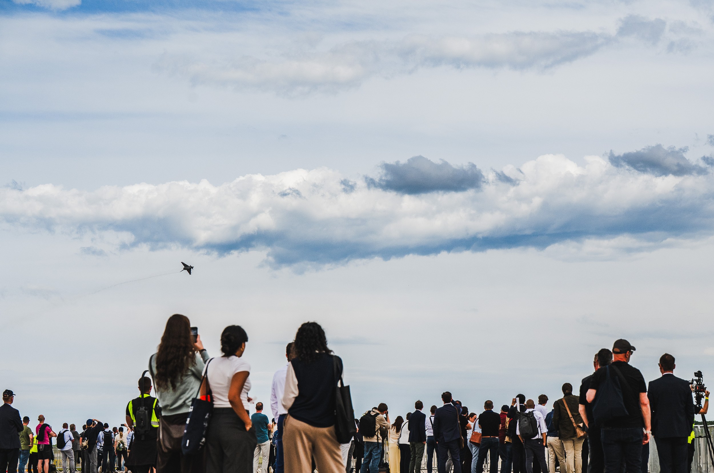 A large crowd watches the flying display at ILA Berlin 2026 from the outdoor grounds, with many people raising …