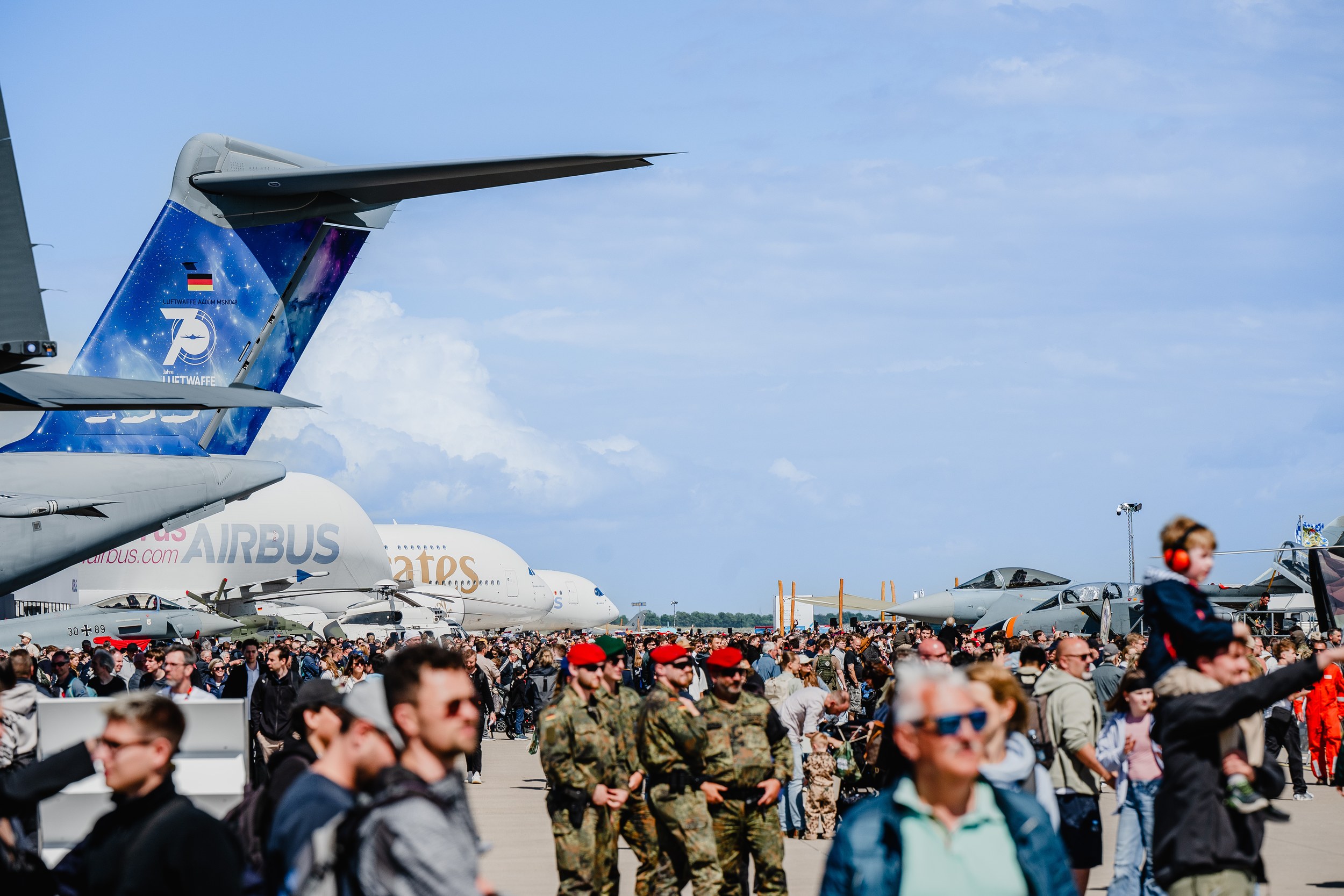A wide outdoor view shows a dense crowd among military and civil aircraft in the static display.